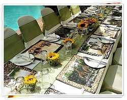 African animal placemats, crockery, cutlery, cream napkins, small glass holders with sunflowers, olive green runners, tiebacks